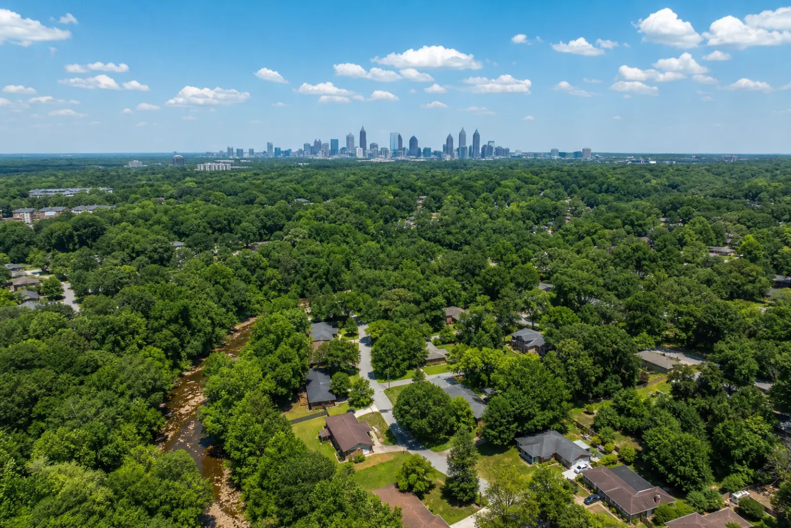 Aerial view at golden hour over southwest Atlanta's rolling tree canopy, rooftops showing through the green, with the downtown skyline on the horizon.